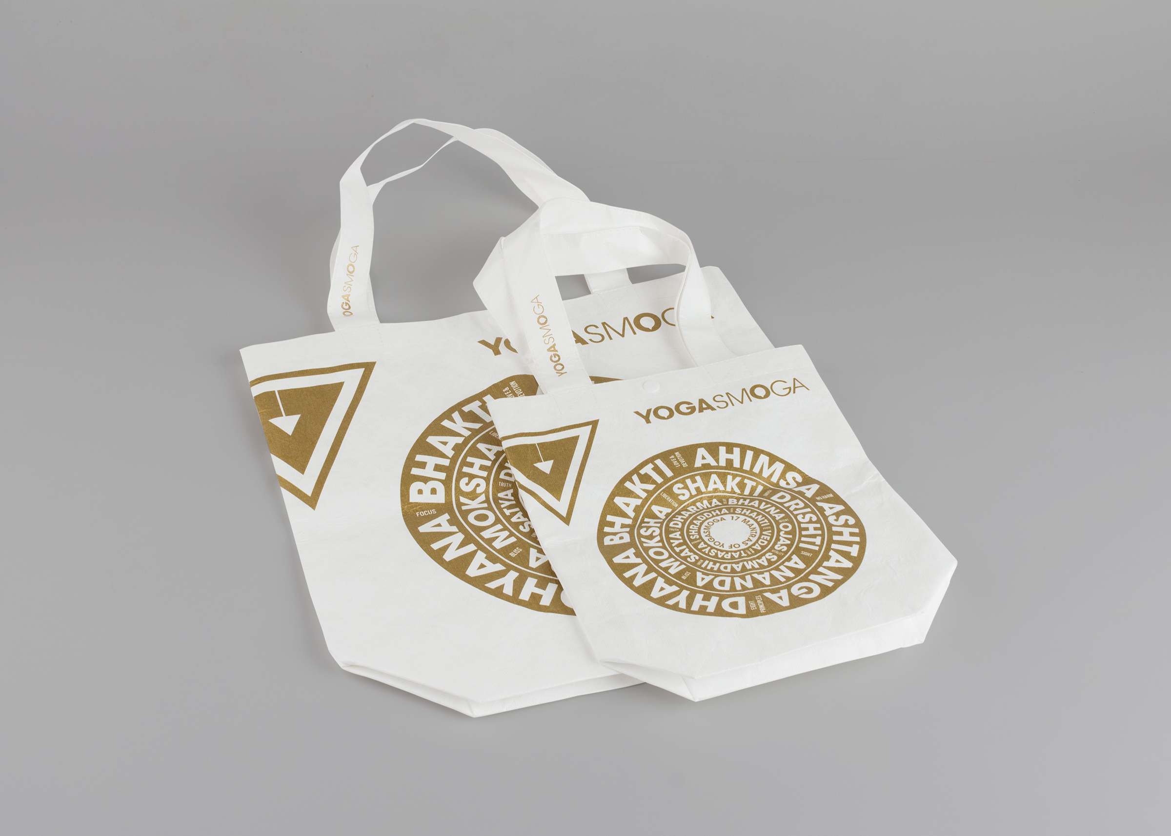 Back of Gold and White YOGASMOGA hoilday retail bags in two sizes, showing Sanskrit words in white arranged in gold background concentric circles.