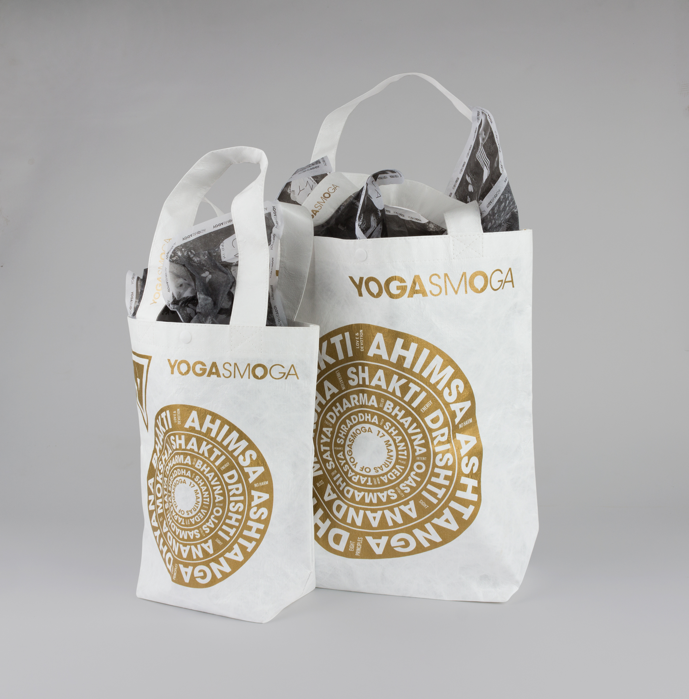Back of Gold and White YOGASMOGA hoilday retail bags in two sizes, showing Sanskrit words in white arranged in gold background concentric circles, lying flat.
